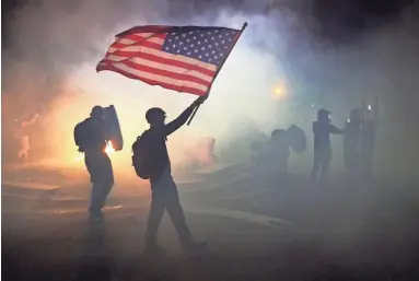  ?? NATHAN HOWARD/GETTY IMAGES ?? A protester waves an American flag while walking through tear gas fired by federal agents early Tuesday during a protest in front of the U.S. Courthouse in Portland.