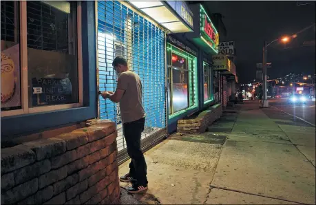  ?? SETH WENIG — THE ASSOCIATED PRESS ?? On a mostly empty street, an employee of Justin’s BBQ closes up for the night Nov. 12in Newark, N.J.