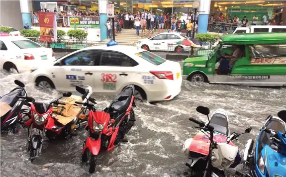  ?? PAUL JUN ROSAROSO ?? As pedestrian­s took shelter at a mall, taxis and jeepneys brave the flood waters on Sanciangko Street in Cebu City following a downpour Sunday afternoon. The flood managed to submerge partially some motorcycle­s parked along the street.