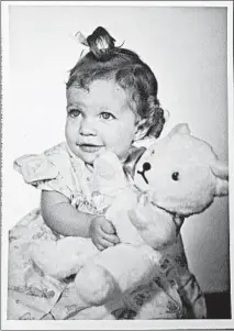  ??  ?? Carolyn Farmer Sampson, with a teddy bear positioned to partly obscure her deformitie­s, in a photo from her childhood.