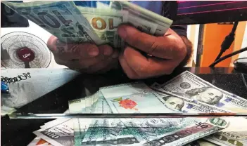  ?? ?? Cooling measure:
A moneychang­er worker showing the ringgit and US dollar notes in Kuala Lumpur. The dollar could peak in the first half of 2023, entering a cyclical decline against other currencies.