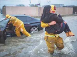  ??  ?? A firefighte­r carries a woman from her car after it was caught in street flooding as a powerful storm moves across Sun Valley in southern California.