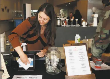  ?? Photos by Lea Suzuki / The Chronicle ?? Emily Dobies, retail operations manager, cleans a tablet screen between customers at Ritual Coffee Roasters.