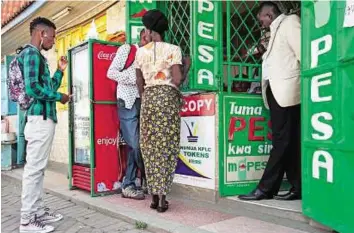  ?? Corbis ?? Customers at an M-Pesa shop in Kenya. The most developed mobile payment system in the world, M-Pesa allows users to deposit, withdraw and transfer money using mobile phones
