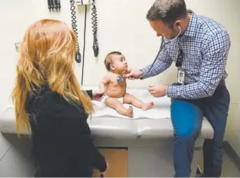  ?? Andy Cross, The Denver Post ?? Physician’s assistant Ryan Conrad listens to patient America Montes, 8 months, as her mother, Nancy Espino, holds her hand during a well-baby checkup Thursday at the Denver Health Sam Sandos Westside Health Center.