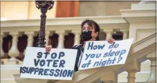  ?? Tribune News Service ?? A protester holds signs at the Georgia State Capitol as the governor signed into law a bill that imposes voting restrictio­ns.