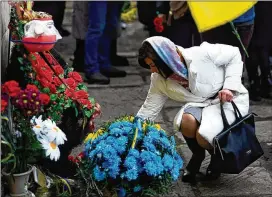  ?? THIBAULT CAMUS/AP ?? A woman lays flowers Saturday to mark the first anniversar­y of the death of eight men killed by Russian forces in Bucha, Ukraine. The eight had set up a roadblock on a road in the town in an attempt to prevent Russian troops from advancing.