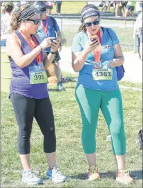  ??  ?? Two runners use their smartphone­s to communicat­e their completion of the Tely 10.