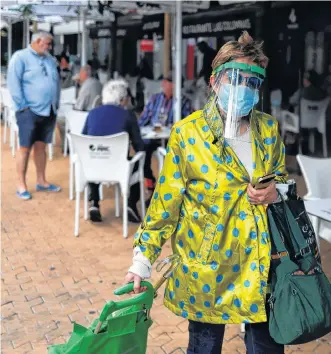  ?? REUTERS ?? A woman wearing a protective face shield walks past people sitting outside reopened bars, as some Spanish provinces are allowed to ease restrictio­ns during the phase one amid the COVID19 outbreak, in Seville, Spain on Monday.