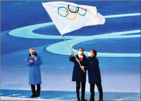  ?? ZHANG WEI / CHINA DAILY ?? Internatio­nal Olympic Committee President Thomas Bach (left) watches as Milan Mayor Giuseppe Sala (center) and Cortina d’Ampezzo Mayor Gianpietro Ghedina hold the Olympic flag during the closing ceremony. The two cities in northern Italy will jointly host the 2026 Winter Olympics.