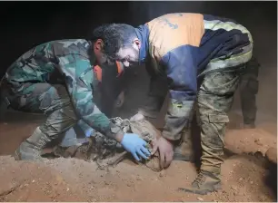  ?? AP ?? Syrian security force members remove human remains at a site where two mass graves are believed to contain the bodies of civilians and troops killed by the daesh militants in the village of Wawi near the northern city of raqqa, Syria. —