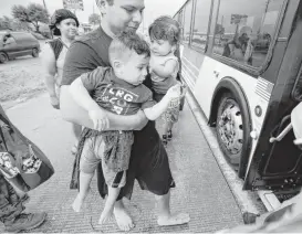  ?? Melissa Phillip / Houston Chronicle ?? A man carries two children as they board a Metro bus Sunday on Interstate 45 S. headed to a shelter at the George R. Brown Convention Center.