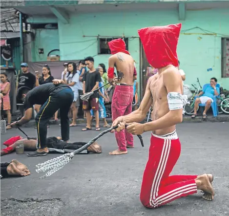  ??  ?? MALE penitents in red hoods whip themselves on a street as residents watch from the sidelines in Mandaluyon­g City, Philippine­s. Despite Catholic Church officials discouragi­ng the tradition, hundreds of Filipinos still practice self-flagellati­on on...