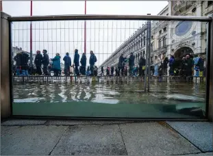  ?? ?? Tourists and residents walk on catwalks Dec. 10 during a sea tide of around 38.18 inches to cross a flooded St. Mark’s Square in Venice where recently installed glass barriers prevent seawater from flooding the 900-yearold iconic St Mark’s Basilica.