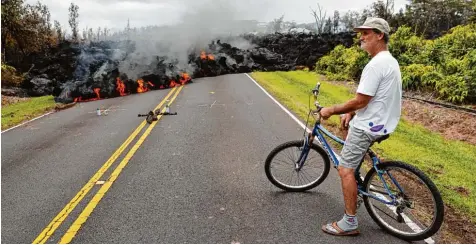  ?? Foto: Marco Garcia, dpa ?? Ein Lavastrom schiebt sich auf Big Island, der größten Insel des US Bundesstaa­ts Hawaii, über eine Straße. Dieser Mann hat sein Haus gleich in der Nähe und hofft, dass die Lava es nicht erreicht.