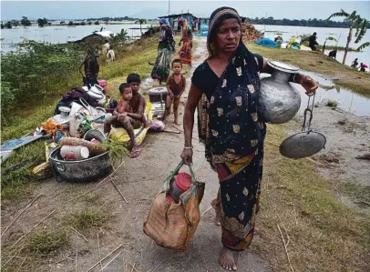  ?? Pictures: AP PHOTO/AFP ?? An Indian woman carries her belongings on an embankment to take shelter in Pabhokathi village east of Gauhati, India, on Monday. Three rivers are overflowin­g in northeaste­rn India and submerging parts of the region, affecting the lives of more than 2 million, officials said on Monday.