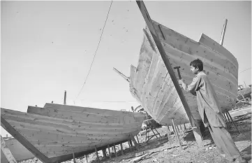  ??  ?? A Pakistani carpenter builds a fishing boat at the harbour in Karachi. Pakistan’s home-grown boat manufactur­ing produces hundreds of boats every year to meet the demands of the local fishing industry. — AFP photo