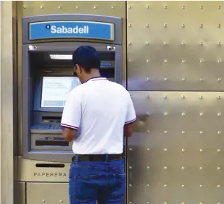  ??  ?? A man withdraws cash from an ATM in Barcelona. Spanish banking stocks have suffered amid a crisis between Madrid and the separatist leaders of Catalonia. (AFP)