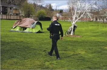  ?? Jenny Kane Associated Press ?? Ore., police officer checks on a homeless person camped in a park on March 23.