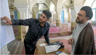  ?? GETTY IMAGES ?? An election official helps a cleric look for the candidates’ codes at a polling station in Qom, south of Tehran.