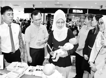  ??  ?? Fatimah (third left) cradles a ‘baby’ at a booth, where she is accompanie­d by (from left) Hii, Dr Toh, Dr Ngian and Ngu.