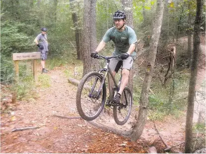  ?? David Hopper ?? Bill Collier, left, watches as Mitch Callihan jumps an obstacle after riding through a creek on the bike trails at the 100 Acre Wood Preserve. The preserve has 2 miles of trails through rolling, forested terrain.