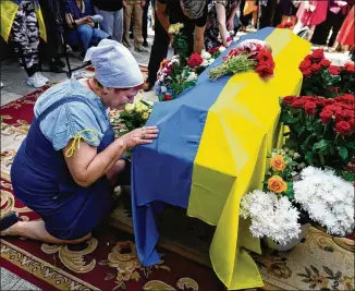  ?? NATACHA PISARENKO/AP ?? A woman kneels at activist and soldier Roman Ratushnyi’s coffin during a memorial service Saturday in Kyiv’s downtown square for the young “symbol of a new Ukraine, of freedom.” He was killed in a battle near Izyum, where Russian and Ukrainian troops are fighting for control of the area.