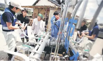  ?? — Reuters photo ?? Local residents receive an emergency water supply in a flooded area in Mabi town in Kurashiki, Okayama Prefecture.