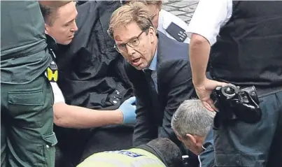  ?? Picture: PA. ?? MP Tobias Ellwood, centre, helps emergency services attend to the police officer.