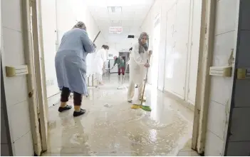  ?? — AFP ?? Employees of the El Kassab hospital in Manouba, on the northeaste­rn outskirts of the capital Tunis, sweep water that flooded part of the building.