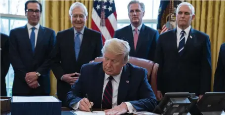  ?? AP ?? PUTTING PEN TO PAPER: President Trump signs the coronaviru­s stimulus relief package at the White House in Washington, D.C., on Friday as Treasury Secretary Steven Mnuchin, Senate Majority Leader Mitch McConnell, House Minority Leader Kevin McCarty, and Vice President Mike Pence watch.