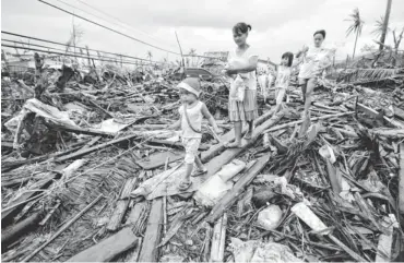  ?? AARON FAVILA, AP ?? Survivors walk through typhoon- ravaged Tacloban, Philippine­s, on Tuesday. The destructio­n left by Typhoon Haiyan highlighte­d a key weakness: fragile infrastruc­ture resulting from decades of neglect.