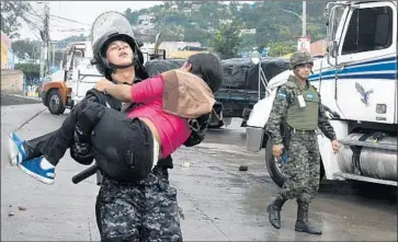  ?? Orlando Sierra AFP/Getty Images ?? A RIOT POLICE officer carries away a woman affected by tear gas during clashes with Nasralla supporters in Tegucigalp­a after Juan Orlando Hernandez was officially declared the winner of last month’s vote.