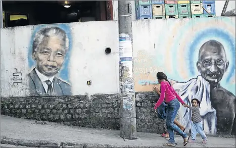  ?? PHOTO: MARIO TAMA/GETTY IMAGES ?? People walk past graffiti depicting civil rights leaders Nelson Mandela of South Africa and Mahatma Gandhi of India in the Babilonia favela, or community in Rio de Janeiro, Brazil. Such individual­s are rare and the seismic events they orchestrat­e visit...