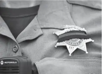  ?? RJ Sangosti, The Denver Post ?? An Adams County sheriff ’s deputy wears a black band across her badge on Thursday after Deputy Heath Gumm was gunned down on Wednesday in Thornton. Gumm was shot in the chest by a suspect who fired several rounds from a handgun.