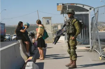  ?? MAYA ALLERUZZO/AP ?? An Israeli soldier secures a bus stop while Israeli settlers wait for a ride Thursday at the Gush Etzion transporta­tion hub for a number of West Bank Jewish settlement­s. Israeli settlers in the West Bank could soon face military rule.