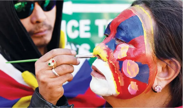  ?? Agence France-presse ?? A woman gets her face painted outside the Dalai Lama’s temple in Mcleod Ganj, India, on Sunday.