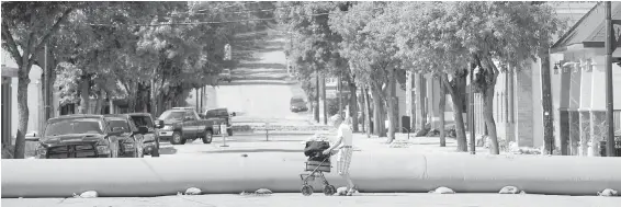  ??  ?? A man walks past a water-filled dike with his luggage on his walker near the Kettle River in the almost deserted town of Grand Forks.