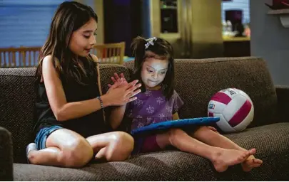  ?? Brett Coomer / Houston Chronicle ?? Six-year-old Miranda Pichardo, who has Down syndrome, high-fives with her sister Paloma, 10, as she plays on an iPad.