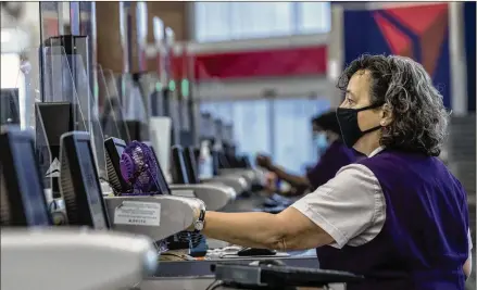  ?? ALYSSA POINTER / ALYSSA.POINTER@AJC.COM ?? A Delta Air Lines employee works behind plexiglass screens as she checks in passengers in the Domestic Terminal at Hartsfield Jackson Internatio­nal Airport in Atlanta last month.