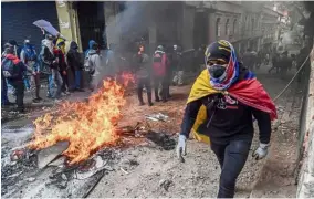  ?? — AFP ?? Fiery: A demonstrat­or wrapped in an Ecuadorean flag walking past a barricade set on fire during clashes with riot police in Quito.