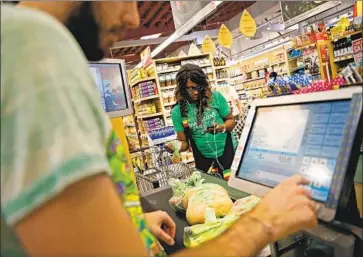  ?? INSTACART SHOPPER Robert Gauthier Los Angeles Times ?? Kara Pete double-checks her cellphone for items ordered by a customer while cashier Jason Ellsworth rings up groceries at a Whole Foods Market in Sherman Oaks in a 2014 photo.