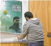  ??  ?? A Syrian man hangs a poster ahead of the screening of Feras Fayyad’s Oscar- nominated film “Last Men in Aleppo” at the University of Idlib on Feb. 12.