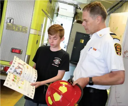  ?? CITIZEN PHOTO BY BRENT BRAATEN ?? Nathan McTaggart shows Prince George Fire Rescue Deputy Chief Cliff Warner his third children’s book, Brandy & Her Super Hero, about the Cariboo forest fires.