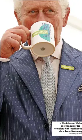 ?? Jacob King/PA wire ?? > The Prince of Wales
enjoys a cup of tea – complete with local honey
– in a Samaritans mug