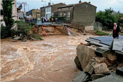  ?? AFP ?? people stand on the road by a bridge over the Trapel River that collapsed after it was hit by heavy rains in France. —