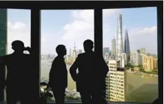  ?? — Reuters ?? People stand near a window overlookin­g the financial district in Shanghai.