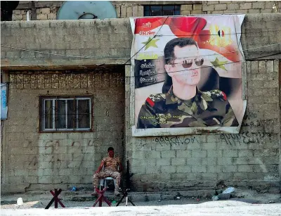  ??  ?? Venti di guerra in Medio Oriente. Un soldato siriano seduto sotto al poster di Assad, a Douma. Appoggiato al muro il Kalashniko­v