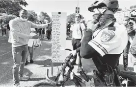  ?? AMY DAVIS/BALTIMORE SUN ?? Westley West holds a sign listing black victims in front of officer Ariel Font on June 1.