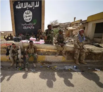  ?? Reuters ?? Shiite Popular Mobilisati­on Forces relax beneath the black flag commonly used by ISIL fighters after yesterday clearing the last of the group’s militants from the Iraqi city of Hawija